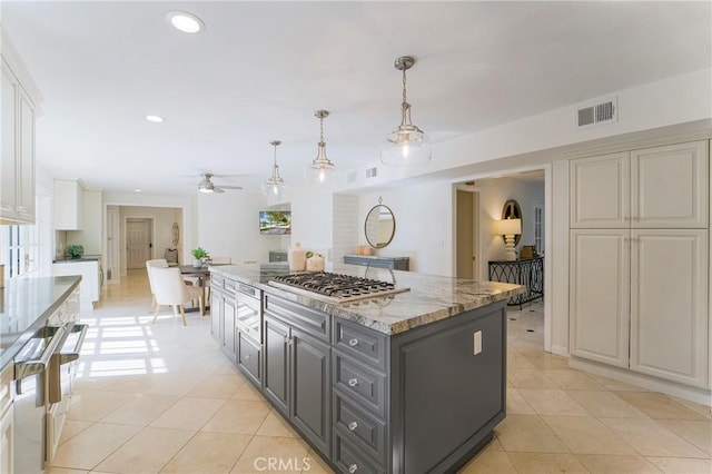 kitchen with light tile patterned floors, a kitchen island, gray cabinets, stainless steel gas stovetop, and white cabinetry