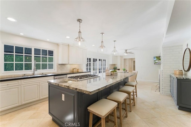 kitchen with backsplash, a kitchen island, light stone countertops, a ceiling fan, and a sink