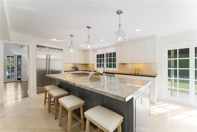 kitchen with tasteful backsplash, a kitchen island, light stone countertops, white cabinets, and stainless steel appliances