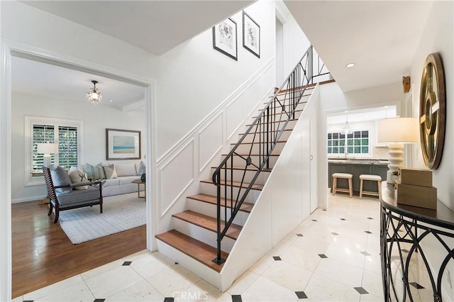 staircase with tile patterned floors, a decorative wall, a notable chandelier, and recessed lighting