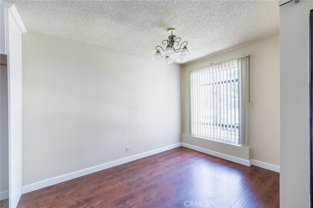 unfurnished room with baseboards, dark wood-type flooring, a textured ceiling, and an inviting chandelier