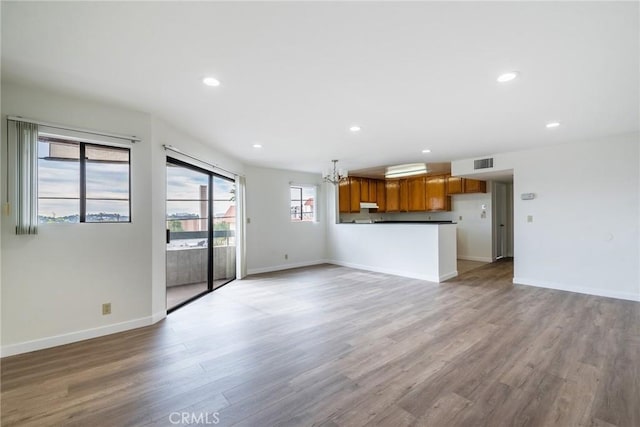 unfurnished living room featuring light wood-type flooring, baseboards, visible vents, and a chandelier