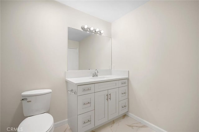 half bath with toilet, marble finish floor, baseboards, and vanity