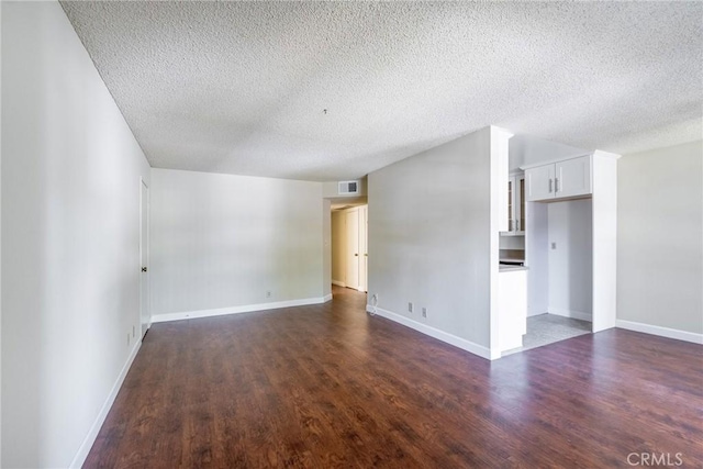 unfurnished room featuring dark wood-style flooring, visible vents, and baseboards