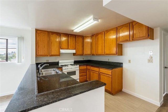 kitchen featuring brown cabinets, white gas range, a sink, dark stone counters, and under cabinet range hood