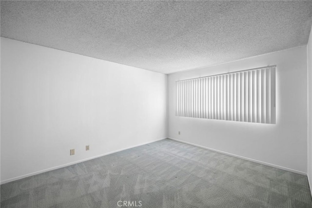 carpeted spare room featuring a textured ceiling and baseboards