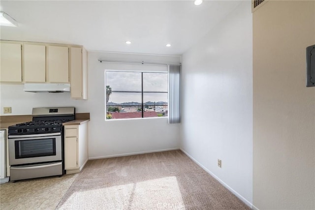 kitchen featuring cream cabinets, light carpet, stainless steel gas range oven, under cabinet range hood, and baseboards