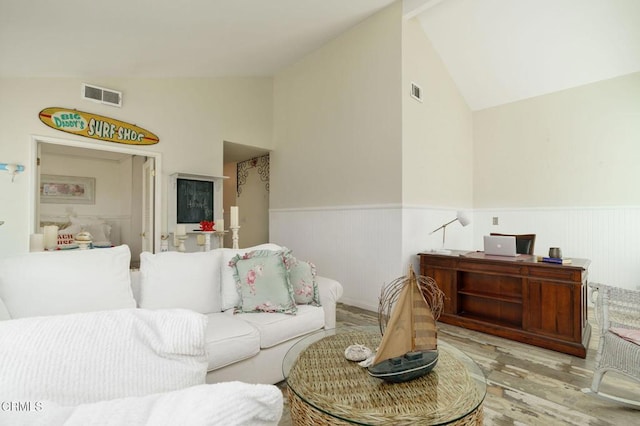 living room with a wainscoted wall, vaulted ceiling, and visible vents