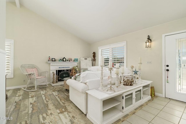 living room with a fireplace with raised hearth, baseboards, vaulted ceiling, and light wood finished floors