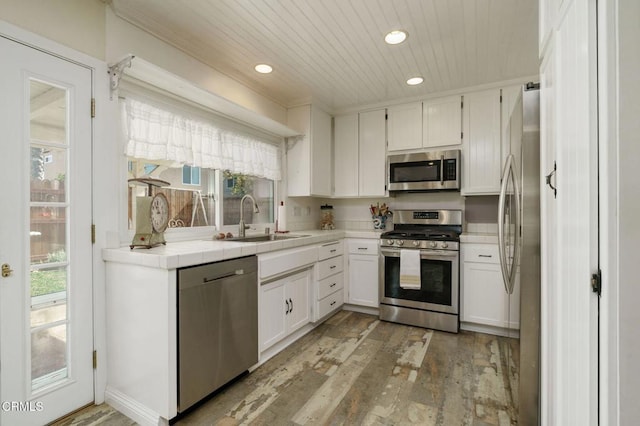 kitchen featuring tile counters, appliances with stainless steel finishes, white cabinets, a sink, and light wood-type flooring