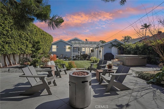 patio terrace at dusk with an outdoor fire pit, a hot tub, grilling area, fence, and a pergola