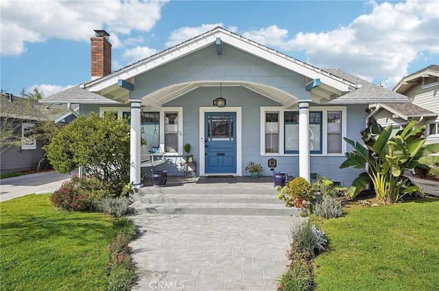 bungalow-style home featuring covered porch, a chimney, and a front yard