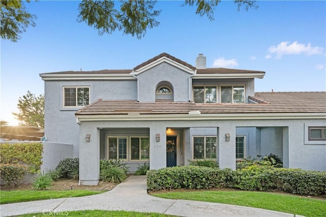 mediterranean / spanish-style house with stucco siding, a chimney, and a tiled roof