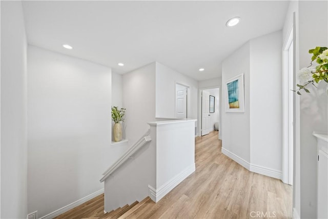 corridor featuring baseboards, light wood finished floors, an upstairs landing, and recessed lighting