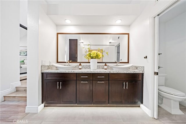 bathroom with double vanity, baseboards, toilet, and a sink