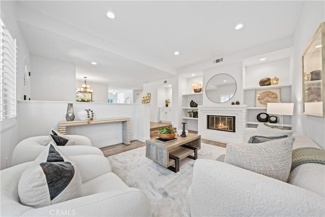 living room with built in shelves, recessed lighting, visible vents, a glass covered fireplace, and wood finished floors