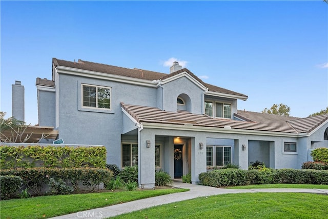 view of front of property with stucco siding, a tiled roof, a chimney, and a front yard