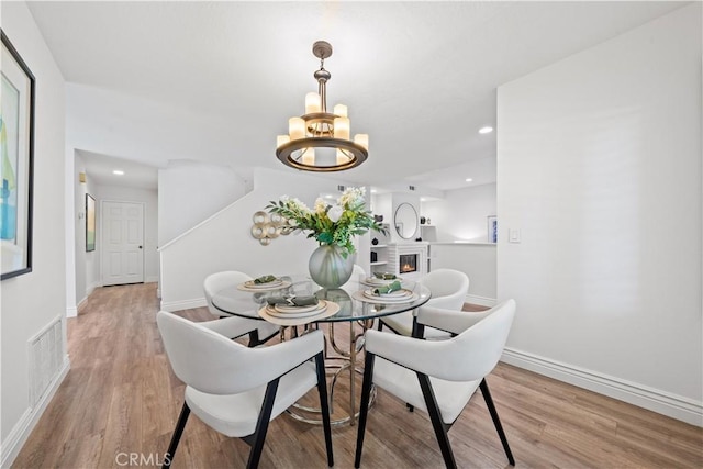 dining space with a warm lit fireplace, a notable chandelier, wood finished floors, visible vents, and baseboards