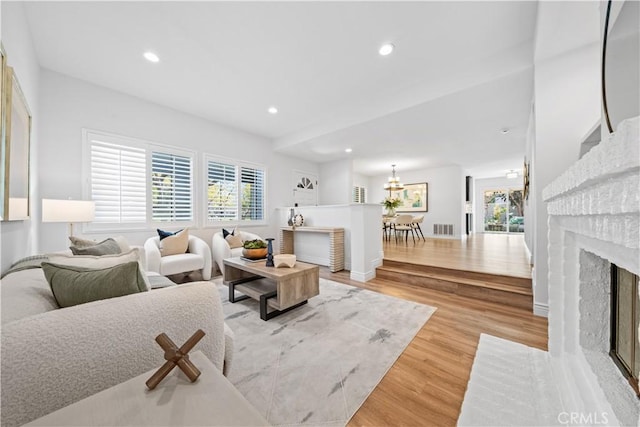 living room with light wood-type flooring, a fireplace, visible vents, and a wealth of natural light