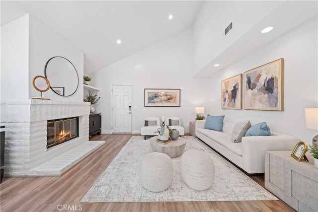 living area featuring a fireplace, recessed lighting, visible vents, wood finished floors, and high vaulted ceiling