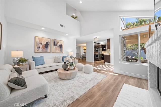 living area with a fireplace, visible vents, light wood-style floors, high vaulted ceiling, and baseboards