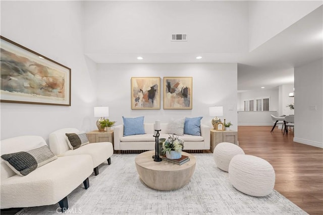 living area with baseboards, visible vents, wood finished floors, a high ceiling, and recessed lighting