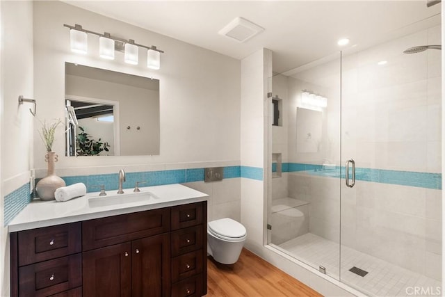 bathroom featuring toilet, wood finished floors, vanity, tile walls, and a shower stall