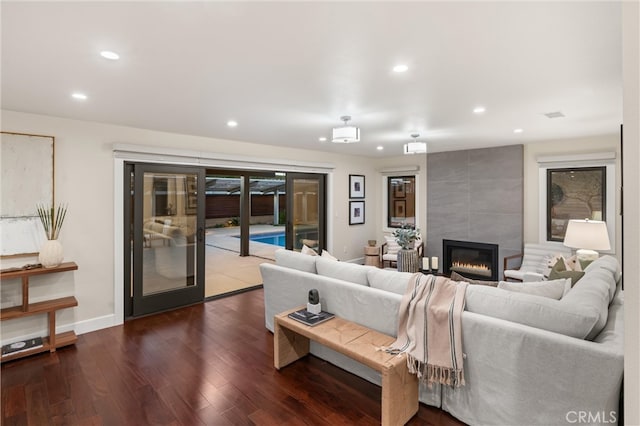 living room featuring baseboards, dark wood-type flooring, a tiled fireplace, and recessed lighting