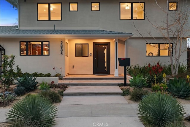 property entrance featuring roof with shingles and stucco siding