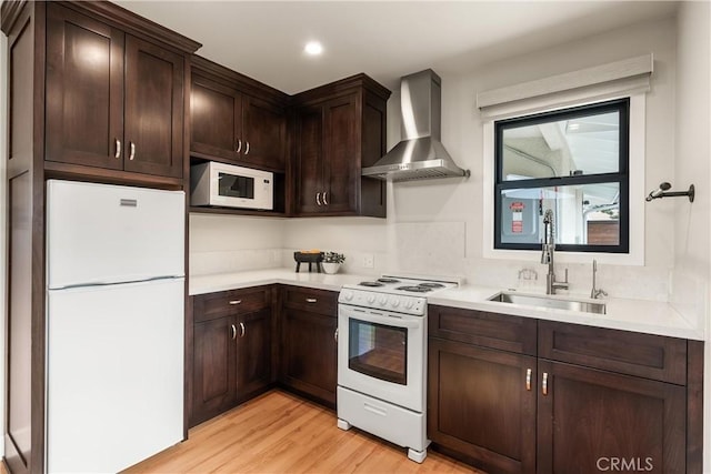 kitchen with white appliances, a sink, wall chimney exhaust hood, and dark brown cabinets