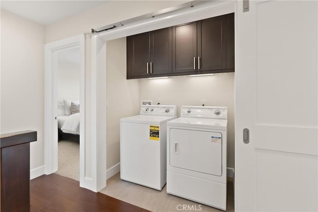 washroom featuring a barn door, baseboards, cabinet space, light wood finished floors, and washing machine and clothes dryer