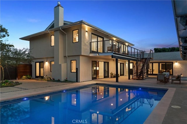 rear view of property featuring stairs, stucco siding, an outdoor pool, a chimney, and a patio area