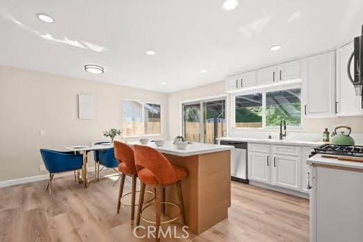 kitchen featuring stainless steel dishwasher, a kitchen bar, a kitchen island, and light wood-style flooring