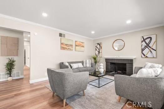 living room with wood finished floors, visible vents, baseboards, ornamental molding, and a brick fireplace