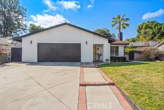 single story home with concrete driveway, an attached garage, fence, a front lawn, and stucco siding