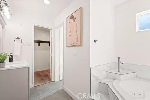 full bath featuring a jetted tub, vanity, a walk in closet, and tile patterned floors