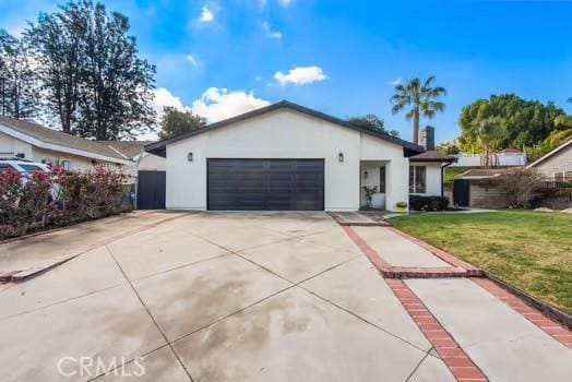 ranch-style home featuring an attached garage, driveway, a front lawn, and stucco siding