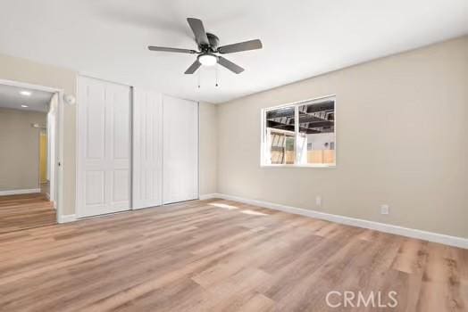 unfurnished bedroom with wood finished floors, two closets, and baseboards