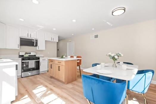 kitchen featuring a breakfast bar area, light wood-style flooring, a kitchen island, light countertops, and appliances with stainless steel finishes