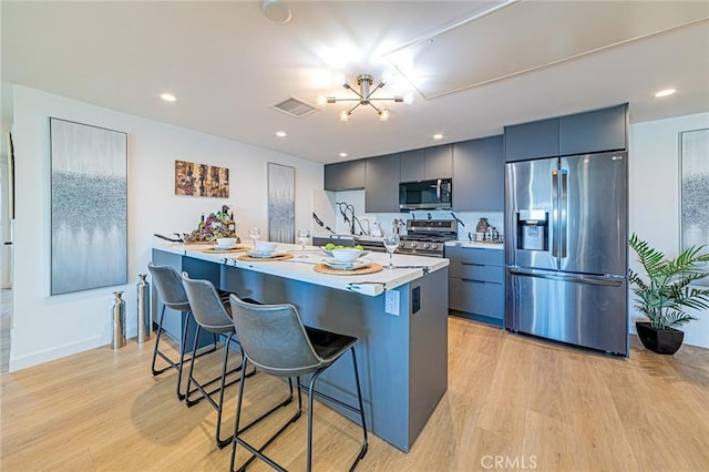 kitchen featuring appliances with stainless steel finishes, a breakfast bar, visible vents, and light wood-style flooring