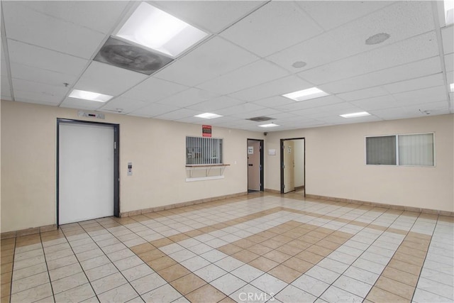 unfurnished room with light tile patterned floors, baseboards, a drop ceiling, and elevator