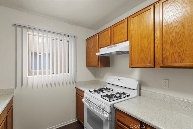 kitchen with light countertops, white range with gas stovetop, brown cabinets, and under cabinet range hood