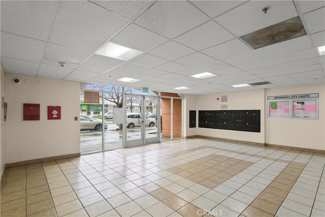 interior space with a drop ceiling, baseboards, and light tile patterned floors