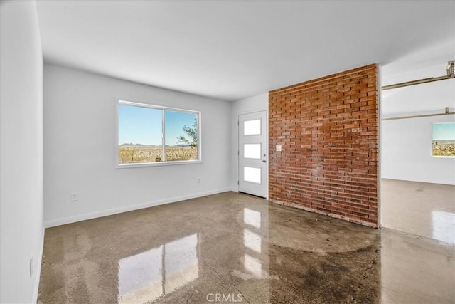 spare room featuring brick wall and baseboards