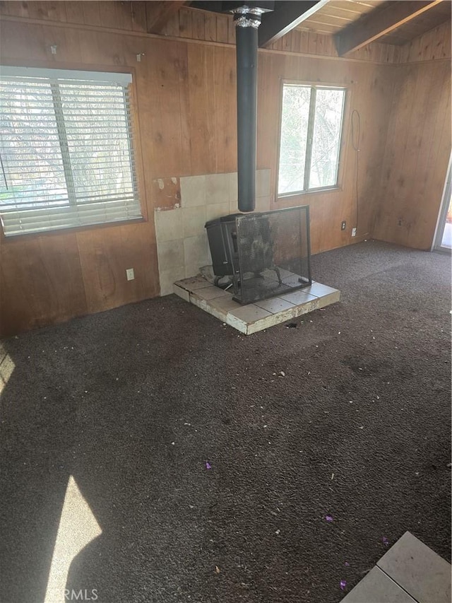 unfurnished living room with carpet, a wood stove, wooden walls, and beam ceiling