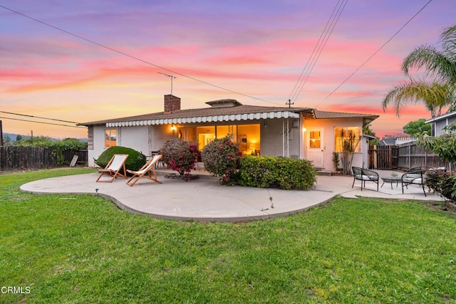 back of house at dusk featuring stucco siding, fence, a lawn, and a patio