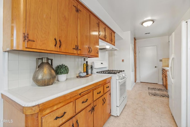 kitchen with white appliances, tasteful backsplash, under cabinet range hood, and brown cabinets