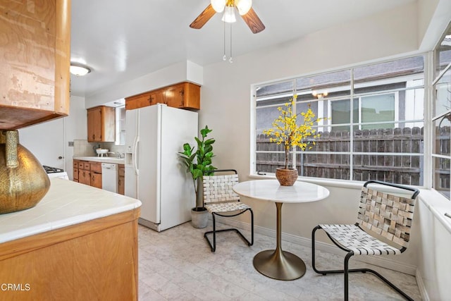 kitchen featuring white appliances, a ceiling fan, tile counters, light floors, and brown cabinetry