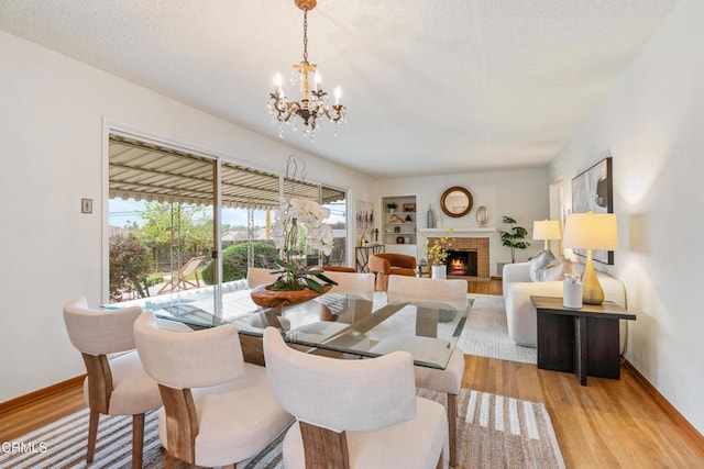 dining area with a notable chandelier, light wood-style flooring, a brick fireplace, a textured ceiling, and baseboards