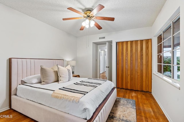 bedroom with a textured ceiling, wood finished floors, visible vents, and baseboards